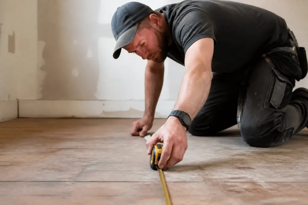 Ouvrier mesurant plancher bois avec metre ruban