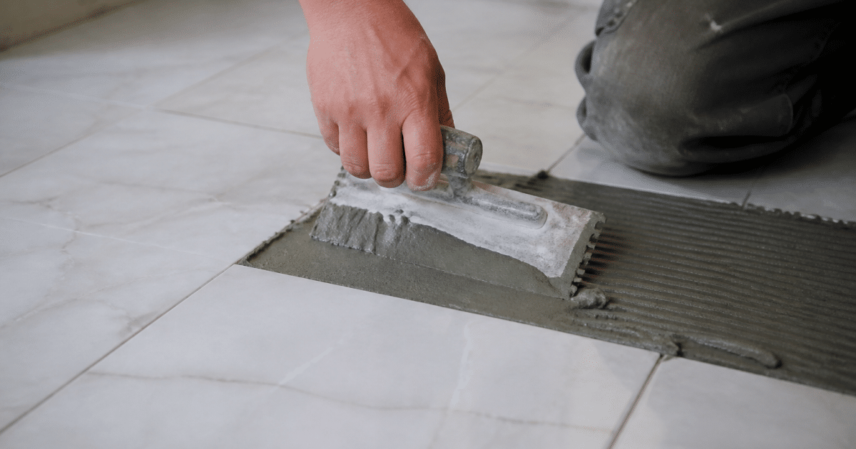 Truelle appliquant colle grise sur carrelage blanc horizontalement