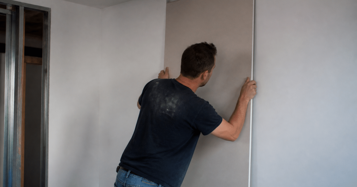 Ouvrier fixant panneau gypse vertical contre surface mur blanc