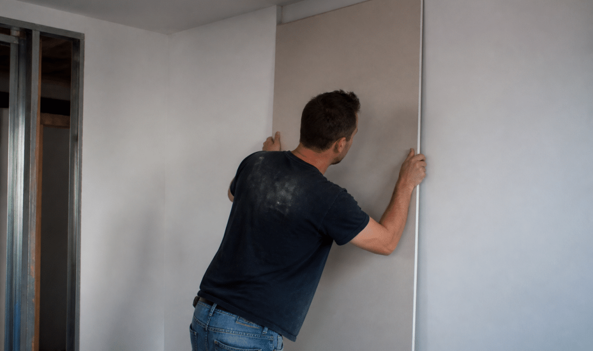 Ouvrier fixant panneau gypse vertical contre surface mur blanc