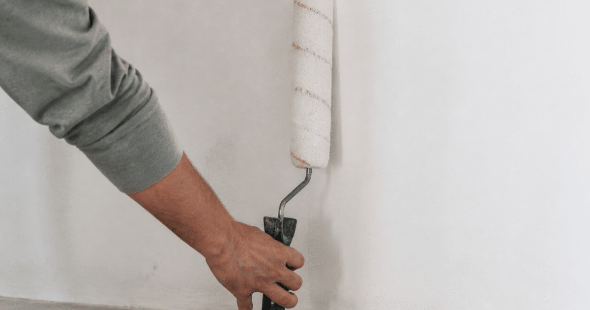 Main tenant rouleau peinture appuyé contre mur blanc verticalement