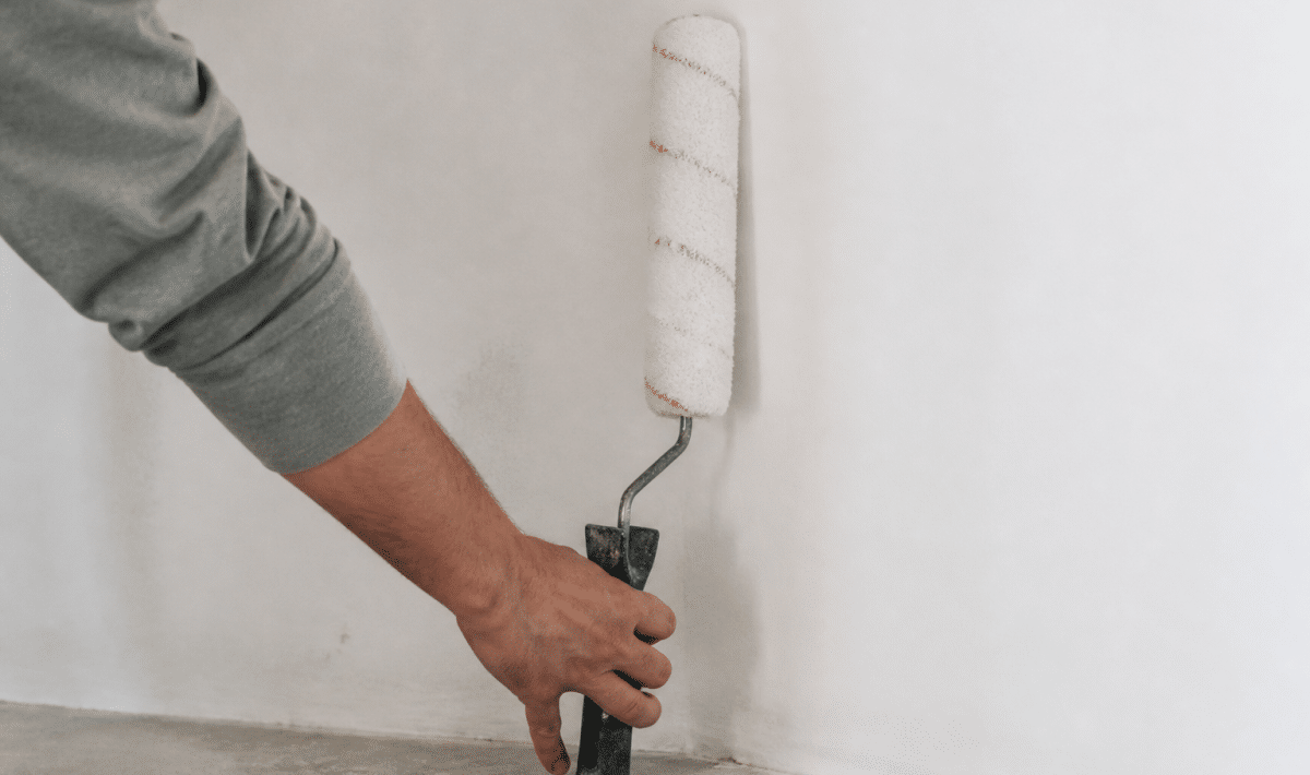 Main tenant rouleau peinture appuyé contre mur blanc verticalement